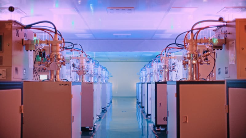 Small reactors with protruding hoses sitting on top of large cabinets stand in a row inside a production facility.